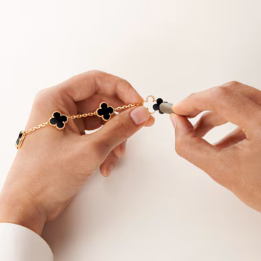 A jeweller's hands using a small tool to set a black clover motif into a gold beaded bracelet
